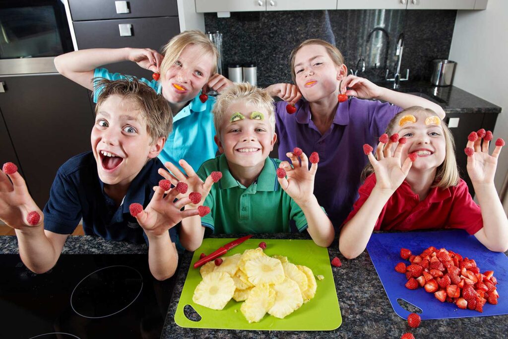 Blije kinderen genieten van schoolfruit in 2025 met vers gesneden fruit zoals aardbeien en ananas, bevorderend voor gezonde voeding op school.